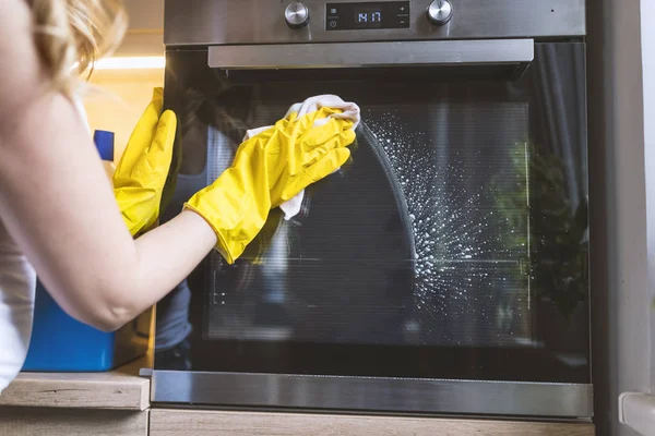 Close up of female hand with yellow protective gloves cleaning oven door. young smiling woman in protective glove with rag cleaning oven. Girl polishing kitchen. People, housework, housekeeping, cleaning concept