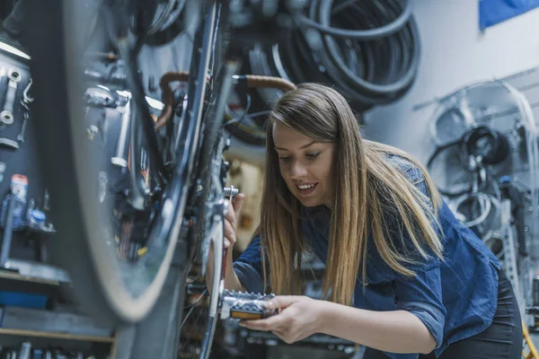 Technician woman fixing bicycle in repair shop.