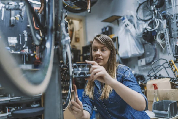 Bike service: mechanic servicewoman installing assembling or adjusting bicycle gear on wheel in workshop.