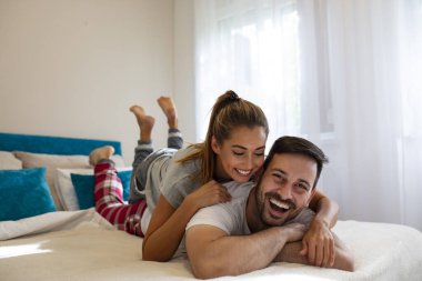 Güzel bir çift öpüşüyor ve pencerenin yanındaki yatak odalarında eğleniyor. Gerçek aşk. Yatak odasında uzanmış gülümseyen genç ve güzel bir çift.. 