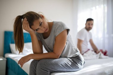 Bir problemimiz var. Genç üzgün kız yatağın kenarında oturuyor, erkek arkadaşına karşı. İlişki sorunları: Genç çiftin sorunları var. Genç çiftin sorunları var..
