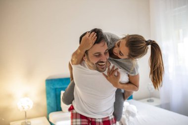 Aşkı kutluyoruz. Genç ve güzel bir çift, erkek kız arkadaşını omuzlarında taşırken evde eğleniyor. Seksi genç çift evde birlikte vakit geçirirken gülümsüyor. Kadın kazma gibi oturuyor.