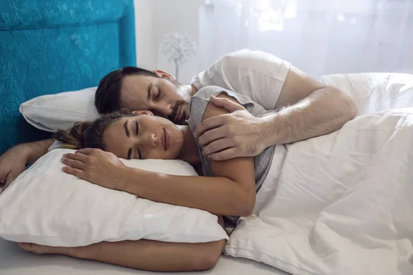 Young couple sleeping in bed under blanket. Young adult couple sleeping peacefully on the bed in bedroom. Young man embracing woman while lying asleep in bed.