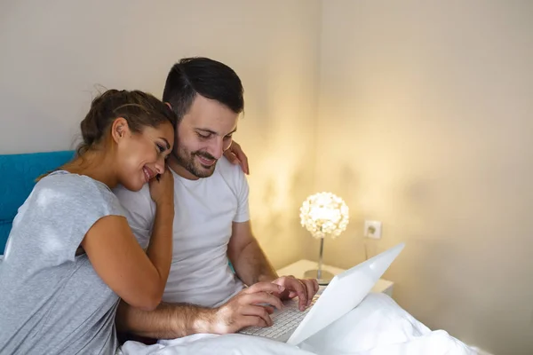 带数字笔记本电脑 屏幕空白的年轻夫妇在家里卧床休息的侧视图 年轻夫妇躺在床上用笔记本电脑 有魅力的女人在床上用笔记本电脑拥抱丈夫 — 图库照片
