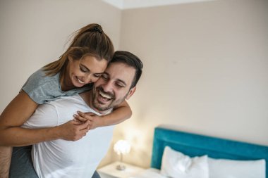 Having fun evde, kız omzunda beyaz yatak odası erkek arkadaşını mutlu heyecanlı genç çift güçlü bin yıllık adam sevgilisi onun sırtında taşıyan eşlerin birlikte komik oyun gülüyor oynayan