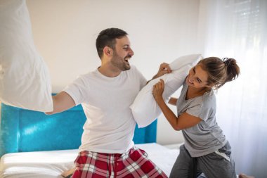 Cheerful funny young couple in love fighting with pillows. Lovely couple in pyjamas spending Valentine's day in their bed, having a pillow fight for entertainment. Couple fighting with pillows
