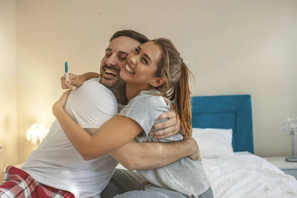 Shot of a happy couple celebrating their new pregnancy at home together.  Young couple looking happy after taking a home pregnancy test. Happy couple looking at pregnancy test on bed at bedroom