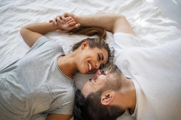 Pretty female looking at her boyfriend in bed stock photo. Overhead close up of young couple lying in bed together. Romantic couple in love looking at each other.. Top view of smiling young couple cuddling in bed in morning.