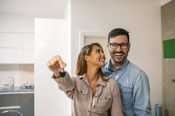 Couple with keys to new home. Cheerful young couple holding keys and smiling while standing in their new house. Happy couple in their new home holding key