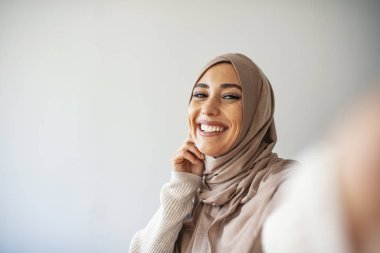 Kafkasyalı Müslüman bir kadın selfie çekiyor. Fularlı mutlu güzel kadın akıllı telefon kullanarak kendi fotoğrafını çekiyor. Genç, güzel ve modern Müslüman bir kadın selfie çekiyor.. 