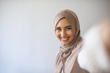 Kafkasyalı Müslüman bir kadın selfie çekiyor. Fularlı mutlu güzel kadın akıllı telefon kullanarak kendi fotoğrafını çekiyor. Genç, güzel ve modern Müslüman bir kadın selfie çekiyor.. 