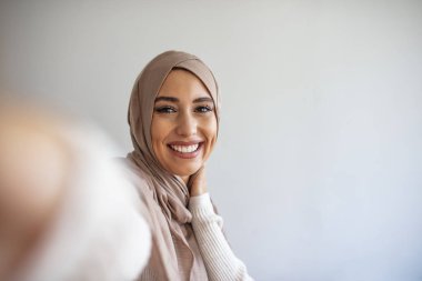 Mutlu genç Müslüman kadın evde cep telefonuyla kendi portresini çekiyor. Cep telefonuyla tesettürlü mutlu bir Arap kadın selfie çekiyor. Gülümseyen kızın portresi, poz vermek.