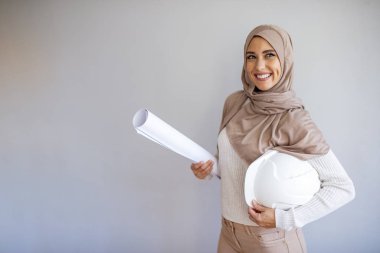 Gri arka planda koruyucu kask takan genç Müslüman mimar kadın. Stüdyoda izole edilmiş güzel bir Arap mimar kadın. Koruyucu miğfer tutan, tesettürlü usta Arap Müslüman kadın..