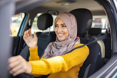 Başörtülü genç Asyalı Müslüman kadın arabanın içinde gülümsüyor. Güzel, beyaz, Müslüman bir kadın, bir araba çekiminde hafif tesettüre bürünmüş. Güzel Müslüman kadın, dişlek gülüşlü araba kullanıyor.. 