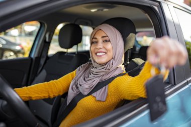 Yeni bir araçta arabanın anahtarını tutan mutlu bir Arap kadını. Müslüman kadın yeni arabasında. Yeni aracın içinde arabanın anahtarını tutan mutlu Arap kadın. Arabada oturan Müslüman Kadın