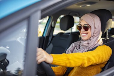 Genç Müslüman kadın sürücü. Gülümseyen Müslüman kadın aracını kullanıyor. Araba kullanan tesettürlü Müslüman bir kadın. Faslı bir kadın kullanıyor. Müslüman kadın yeni arabasında 