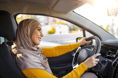 Güzel Müslüman kadın tesettürlü araba kullanıyor. Emirati kadını gün batımında Dubai 'de araba kullanıyor. Orta Doğulu araba kullanan bir kadının portresi, modern bej bir Abaya giyiyor..