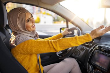 Arabayı süren ve birine bağıran müslüman kadın hoşnutsuzdu. Kızgın Müslüman kadın sürücü öfkesi. Kızgın şoför. Kızgın genç kadın araba kullanırken bağırıyor ve el kol hareketi yapıyor.