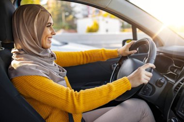 Gün batımında yeni arabasını süren güzel, mutlu, gülümseyen Müslüman kadın. Yolculukta genç Müslüman bir kadın, gülümsüyor. Araba kullanan Arap kadınlar. Genç Müslüman kadın sürücü.