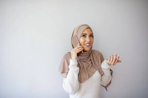 灰色の背景に隔離された携帯電話で話している笑顔の若いアラビア人女性の肖像画 その日を楽しみながら携帯電話で話す若いイスラム教徒の女性の笑顔 — ストック写真