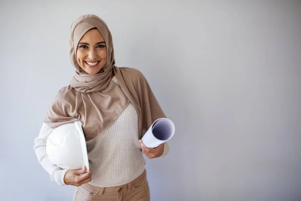 個人的な保護具を持つイスラム教徒の女性 建築家として美しい若いイスラム教徒の女性 設計図付きの若い女性の建設専門家 灰色の背景に隔離されたイスラム教徒の女性建築家 — ストック写真