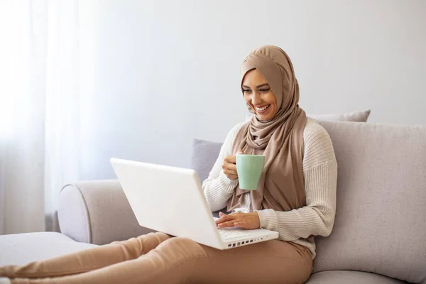 若いアジア系イスラム教徒の女性だけで彼女のラップトップ上で動作し コーヒーマグカップを保持カフェに座っている 白いラップトップを使用して若いイスラム教徒の女性 美しい若いですイスラム教徒女性使用ラップトップで自宅 — ストック写真