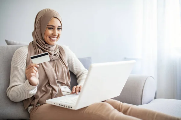 Arab woman making online purchase on laptop. Portrait of happy woman purchasing product via online shopping. Pay using credit card. Muslim woman online shopping