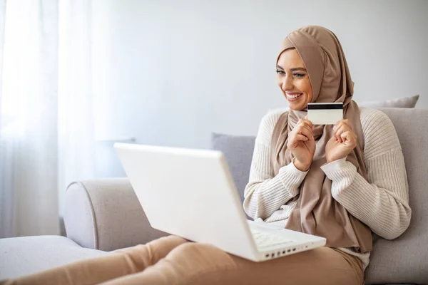 クレジットカードを持っている美しいイスラム教徒の女性 イスラム教徒のビジネス女性は自宅でクレジットカードで買い物をします 魅力的な女性アラビア語保持クレジットカードの作物のショットとオンラインショッピングや支払いのためのラップトップを使用して — ストック写真