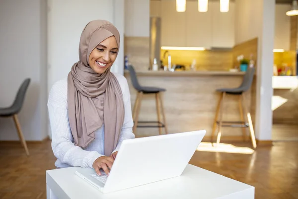 イスラム教徒の女性はコンピュータで働いている 自宅の机に座ってノートパソコンやコーヒーや紅茶を飲んでいるアラブの若いビジネス女性 イスラム教徒の女性が自宅で働いてコンピュータを使って — ストック写真