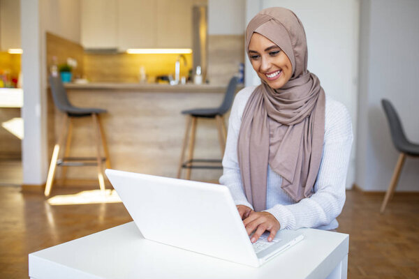 Muslim woman working with computer. Arab Young business woman sitting at her desk at home, working on a laptop computer and drinking coffee or tea. Muslim woman working at a home and using computer.