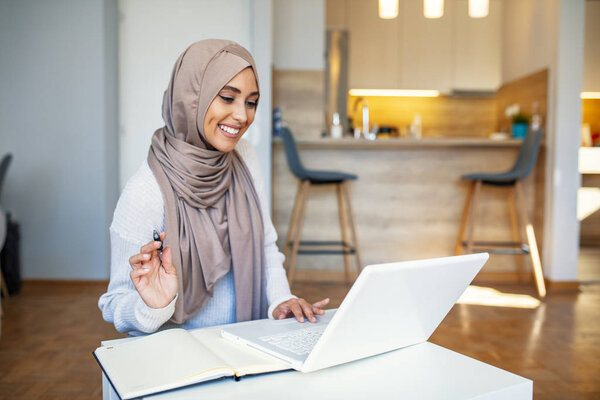 Young saudi business woman working in at home, pointing on laptop, copy space. Muslim female working with computer in the room , writing paper. Young muslim woman using laptop