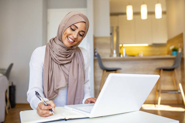 Attractive female Arabic working on laptop computer and paperworks on desk. Arabian Businesswoman working at home. Dedication and technology. Essential for getting her tasks done