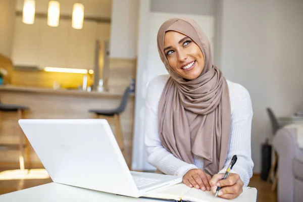 イスラム教徒の女性が自宅で働いている 宗教的なベールを身に着けているアラビア人の女性は 画面を見てキーボードを入力して 彼女のラップトップで働いています 彼女は集中し 様々なソフトウェアやオンラインサービスを使用して喜んでいるようです — ストック写真