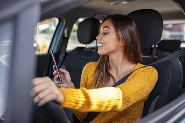 Woman Inside Car Holding Mobile Phone. Young girl is texting in the traffic jam. Young female driver using smart phone at the wheel. Young woman, in car with mobile phone , checking her text message or her navigation