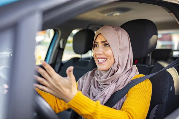 Muslim woman driving and yelling. Negative human emotions face expression. Side profile angry female driver. Angry woman driving a car. The girl with an expression of displeasure is actively gesticulating behind the wheel of the car.