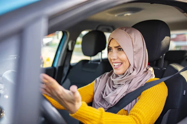 Muslim woman driving and yelling. Negative human emotions face expression. Side profile angry female driver. Angry woman driving a car. The girl with an expression of displeasure is actively gesticulating behind the wheel of the car.