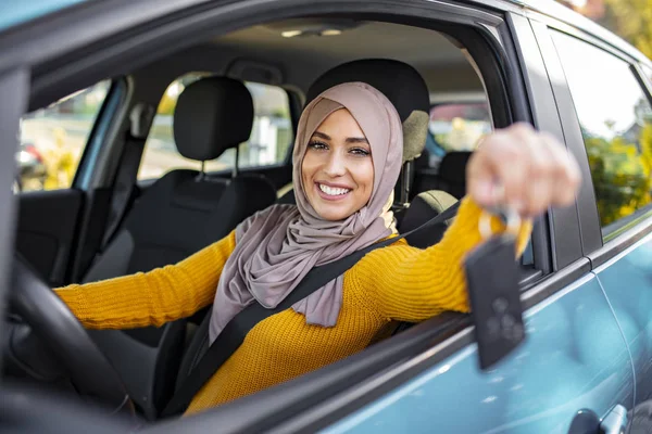 Happy arabian woman holding car key in new vehicle. Muslim woman in her new car. Happy arabian woman holding car key inside new vehicle. Muslim Woman Sitting In Car