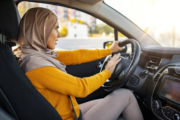 Angry Muslim woman driving a car. The girl with an expression of displeasure is actively gesticulating behind the wheel of the car. Stressed Muslim woman drive car feeling sad and angry.