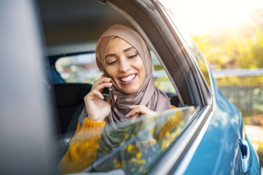 Güzel Müslüman iş kadını iş yerine giderken arabasında. İş kadını, arabada akıllı telefon kullanıyor. Arabadaki akıllı telefonu kullanan Müslüman kadın. 