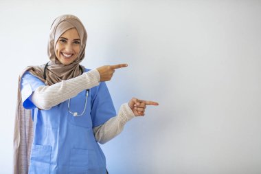 Genç Arap cerrah kadın izole edilmiş arka planda gülümseyen ve kameraya bakıp iki elini ve parmağını yana doğru gösteren. Tıbbî personel kopyalama alanını gösteriyor