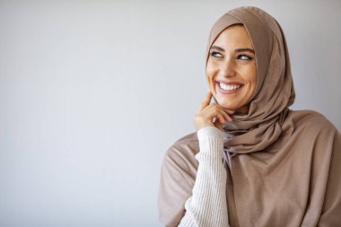 Asyalı genç Müslüman kadın kolları çaprazlanmış bir şekilde başörtüsü ile gülümsüyor. Gri arka planda başörtüsü takan genç Müslüman kadın portresi. Gri arkaplanda güzel Müslüman kadın portresi