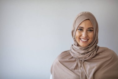Asyalı genç Müslüman kadın kolları çaprazlanmış bir şekilde başörtüsü ile gülümsüyor. Gri arka planda başörtüsü takan genç Müslüman kadın portresi. Gri arkaplanda güzel Müslüman kadın portresi