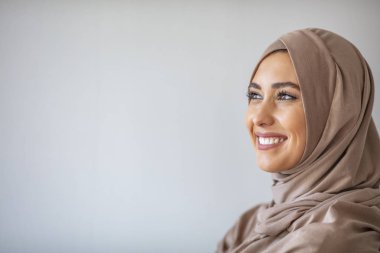 Başörtüsü gülüşlü güzel Asyalı müslüman kadın portresi. 20 'li yaşlarda, tesettürlü, gri arka planda sırıtan müslüman bir kadının portresi.. 