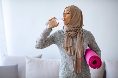 Genç Müslüman kadın koşmaya hazır. İslami kadın spor yaptıktan sonra dinleniyor ve su içiyor. Sağlıklı, tesettürlü, yoga dersine hazır sporcu bir kadın.. 