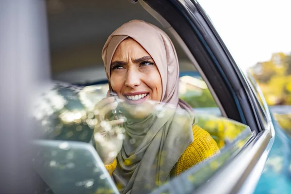 Young Muslim businesswoman talking on the phone in the back seat of the car and holding in hand a digital tablet. Beautiful Muslim business woman in car.
