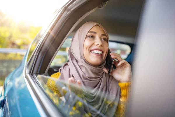 若いイスラム教徒のビジネス女性が車の中で座っている 車の中に座って電話で話している彼女の頭の上にスカーフでイスラム教徒の女の子 車の中でイスラム教徒のビジネス女性 — ストック写真