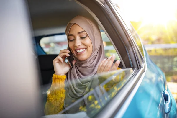 Young muslim business woman sitting in car. Muslim girl with scarf on her head sitting in the car and talking on the phone. Muslim business woman in car.