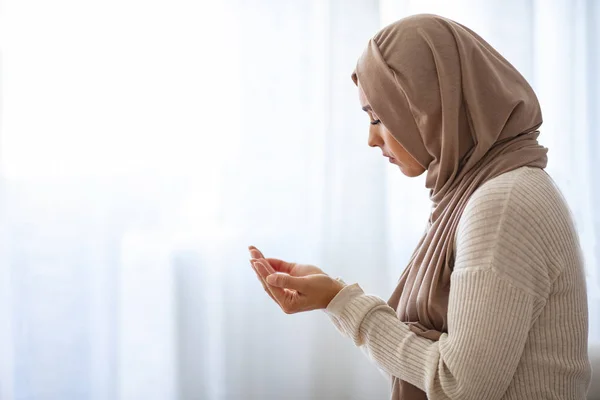Young Woman Praying. Young Muslim woman praying, indoors. Young muslim woman in beige hijab and traditional clothes praying for Allah, copy space. Arab Muslim woman praying