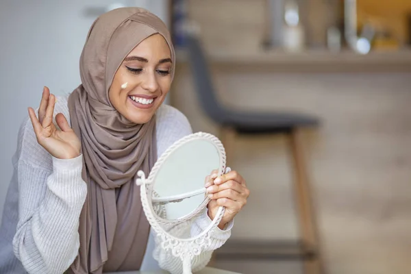 鏡を見ながらクリームを顔に広げているムスリム女性 美の治療だ 女性は顔に保湿剤をつけている 顔にクリームを適用し 鏡を探しているイスラム教徒の女性 — ストック写真