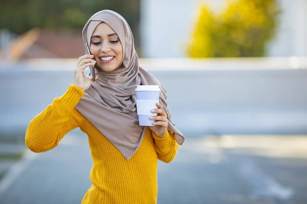 イスラム教徒の女性は晴れた日に屋外にいます 彼女はカジュアルな服と頭のスカーフを着ている 道路の近くに立って 彼女のスマートフォンと話しているイスラム教徒の女性 — ストック写真
